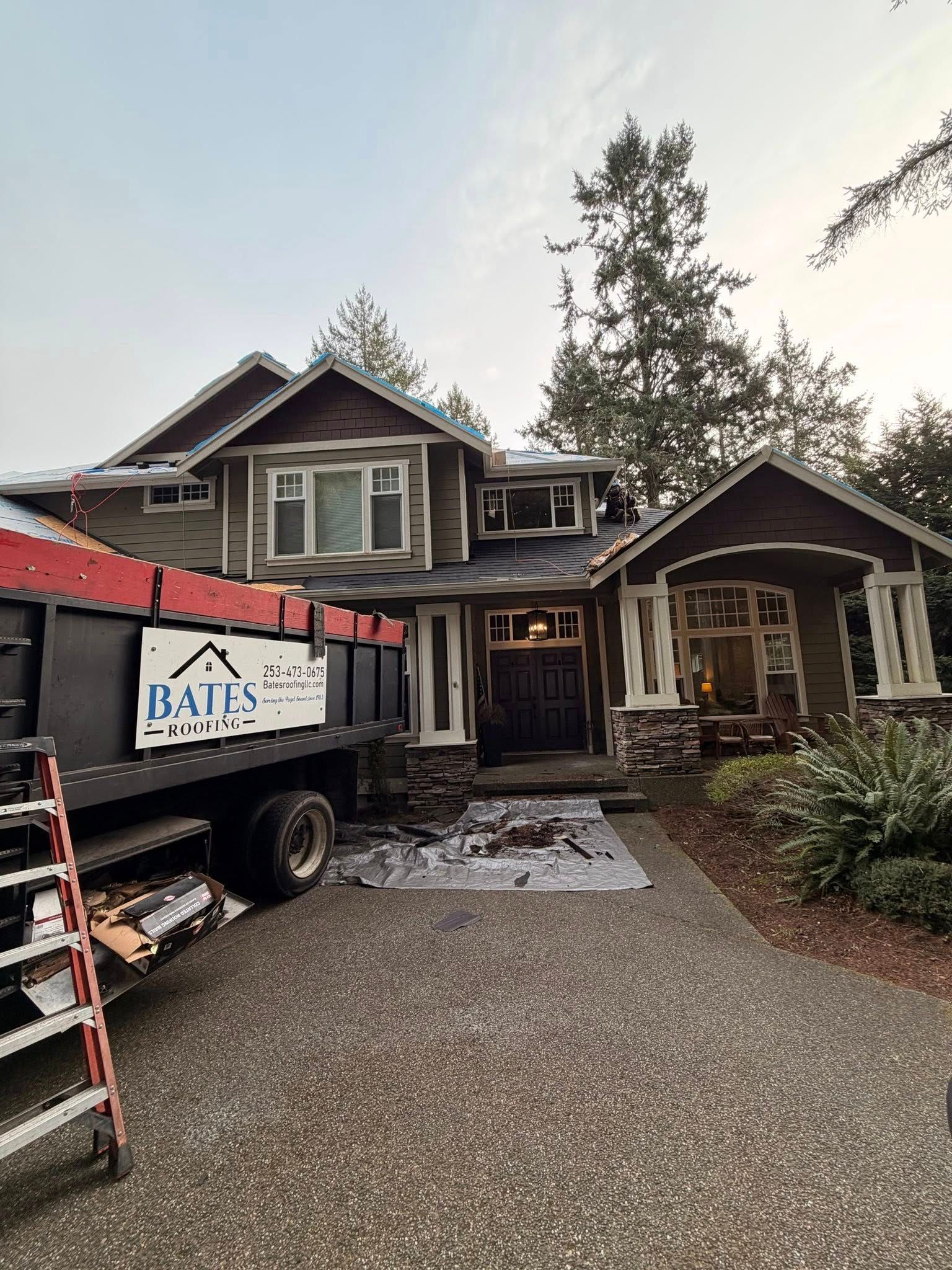 House under construction; roofing debris on driveway, dump truck parked alongside.