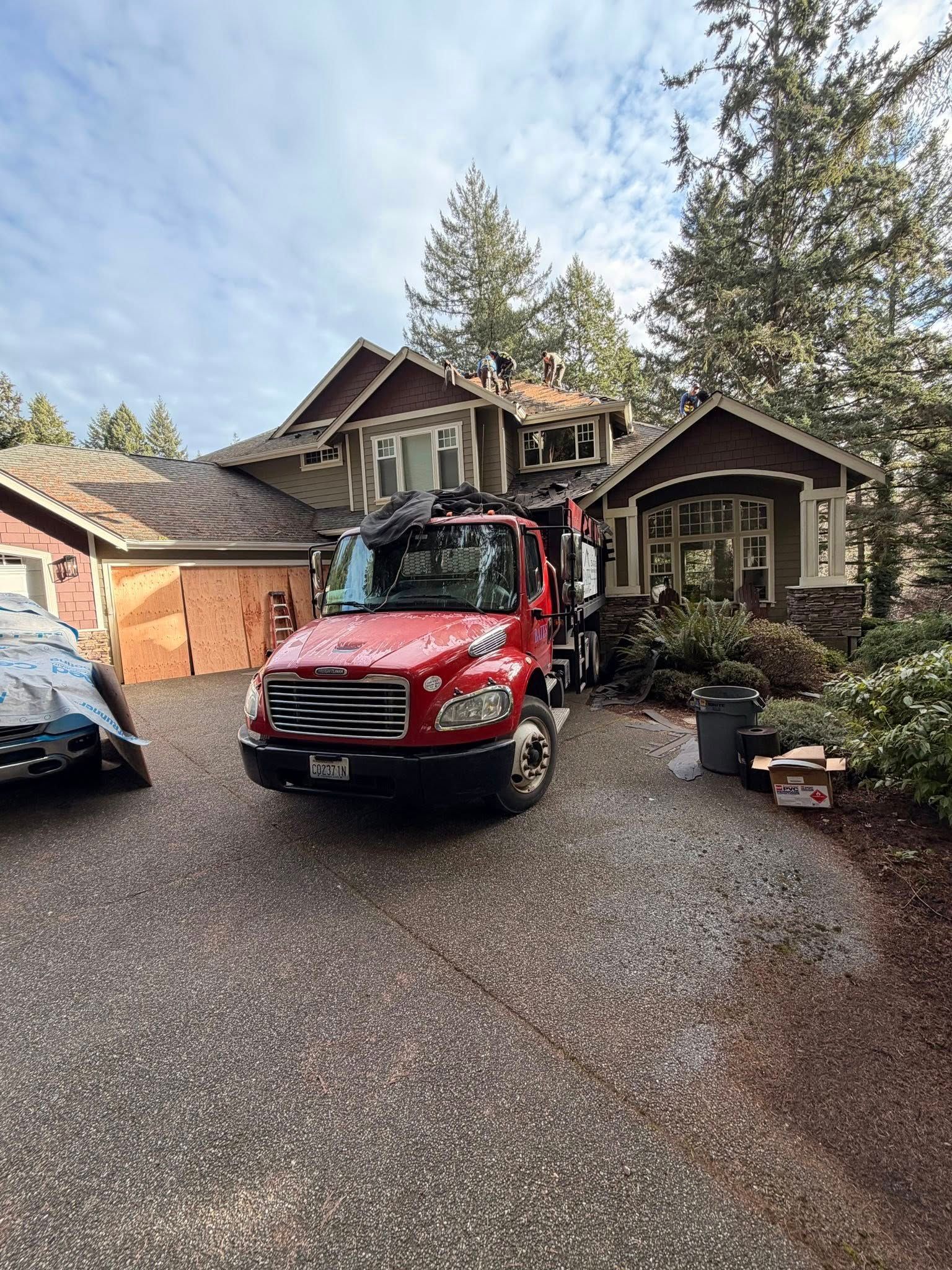 Red truck parked in front of a house. House has multiple rooflines and is surrounded by trees.