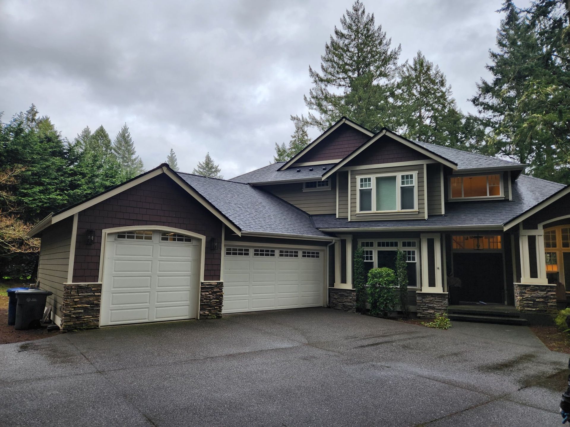 A two-story house with a two-car garage, grey siding, and dark brown accents on an overcast day.