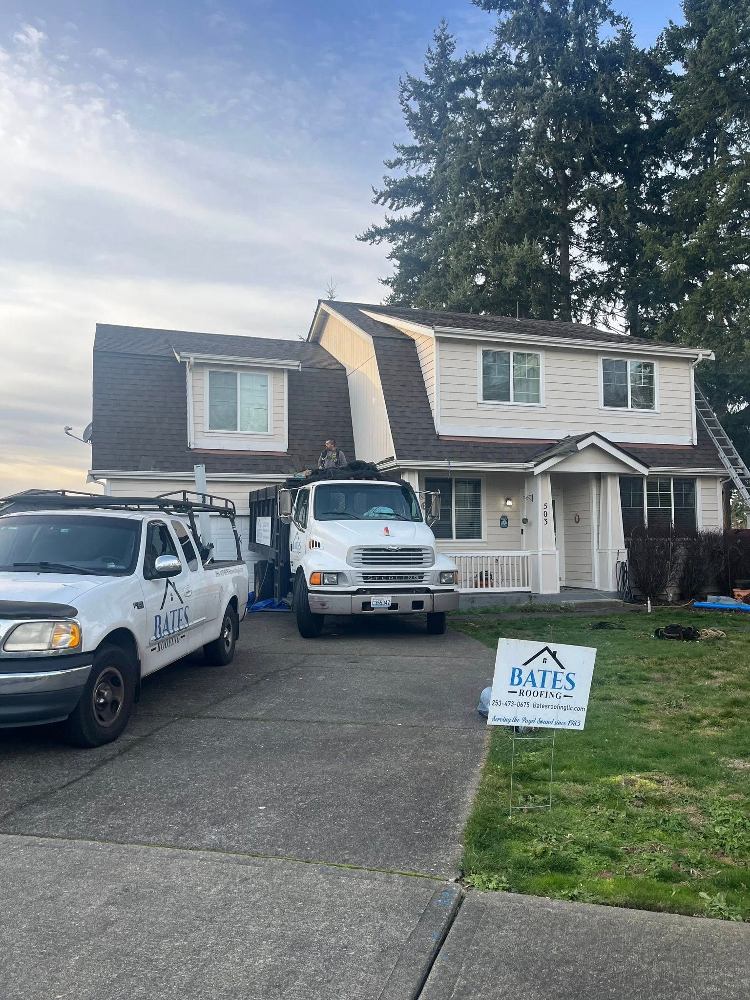 Two work trucks in front of a house. Roofing work is in progress.