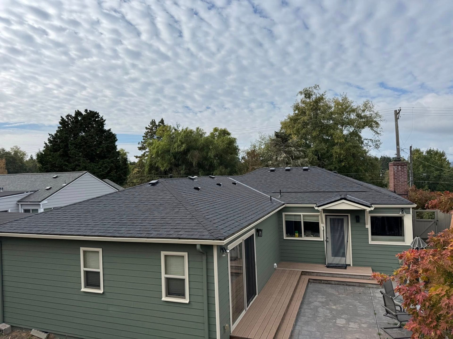 Green house with a dark roof and a cloudy sky.