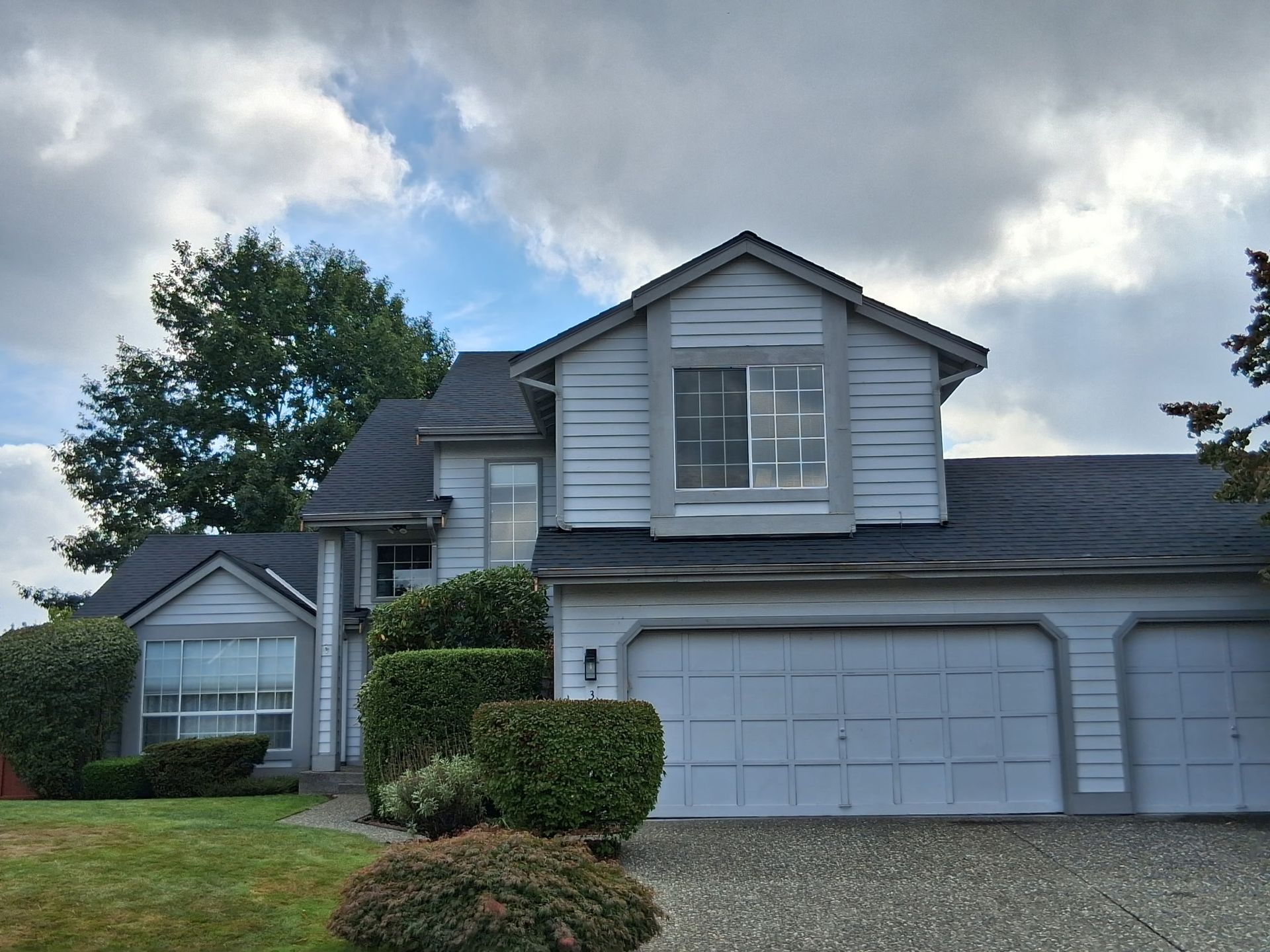 Two-story gray house with a three-car garage, under a cloudy sky.