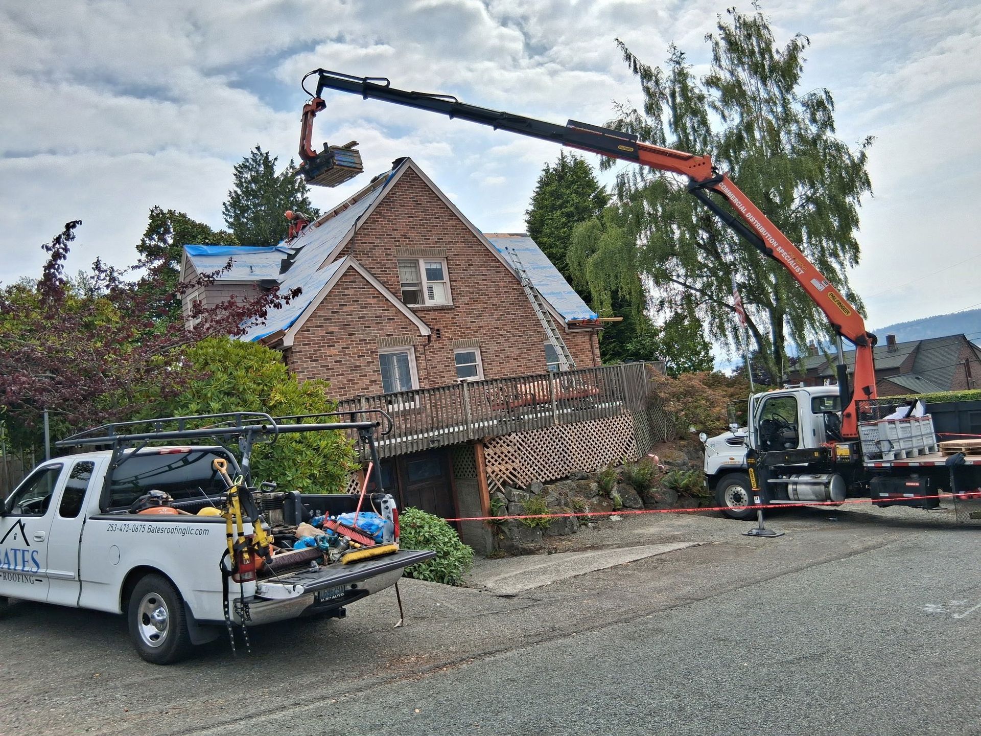 A crane lifting debris from a house roof during construction. A white pickup truck is parked on the driveway.