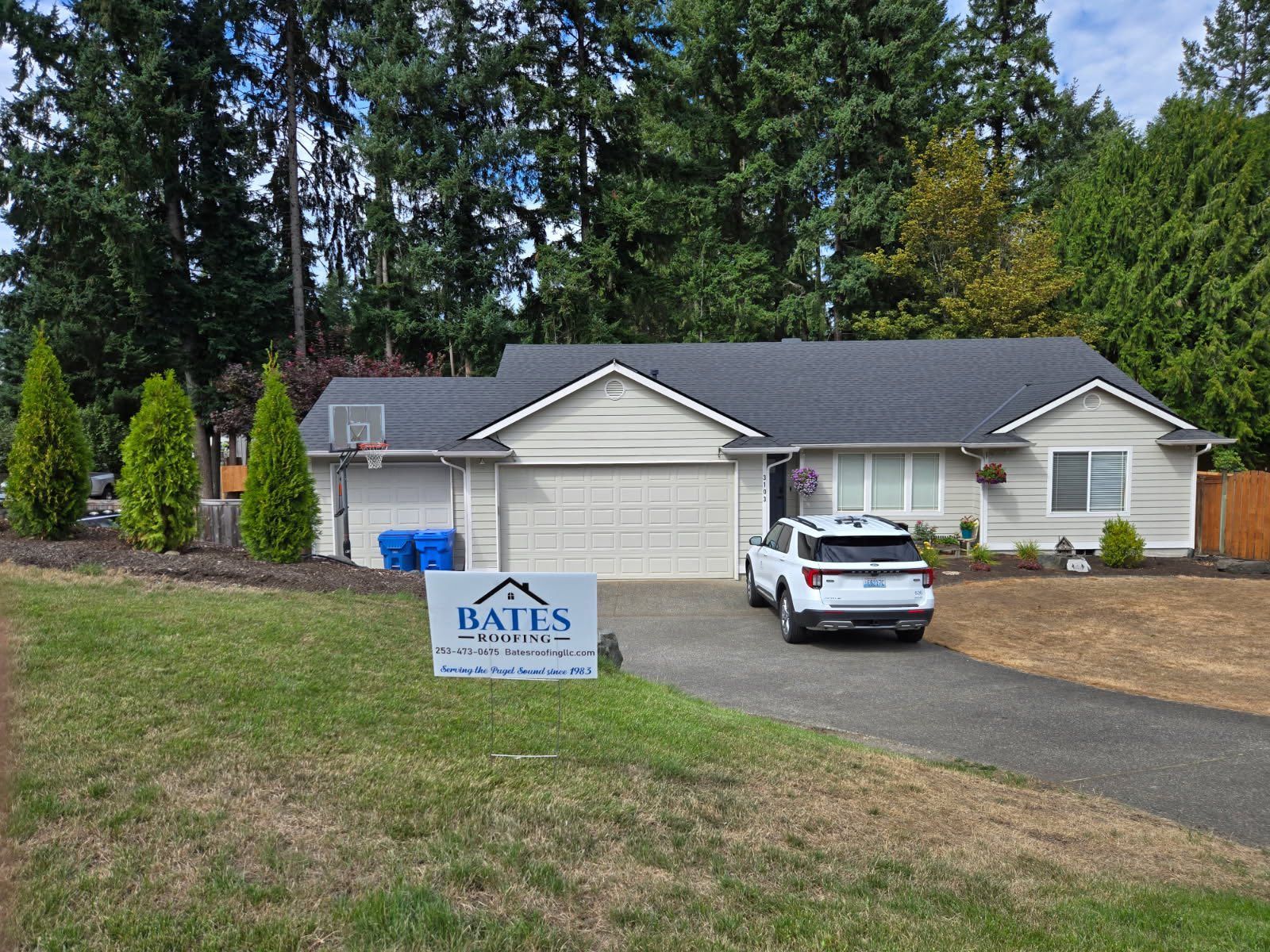 Ranch-style house with a light-colored exterior, driveway, and a sign in the front yard. A white SUV is parked in the driveway.
