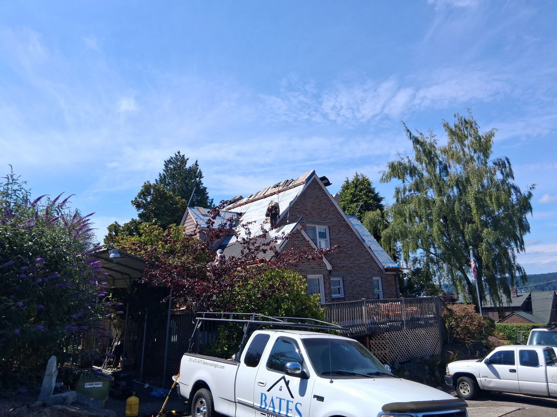 House with damaged roof under blue sky, white work truck parked in front.