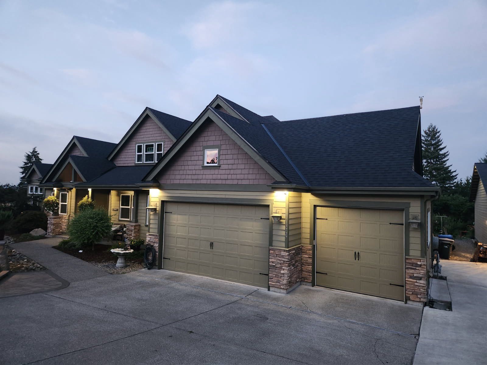 House with two-car garage, brown roof, stone accents, and tan garage doors at dusk.