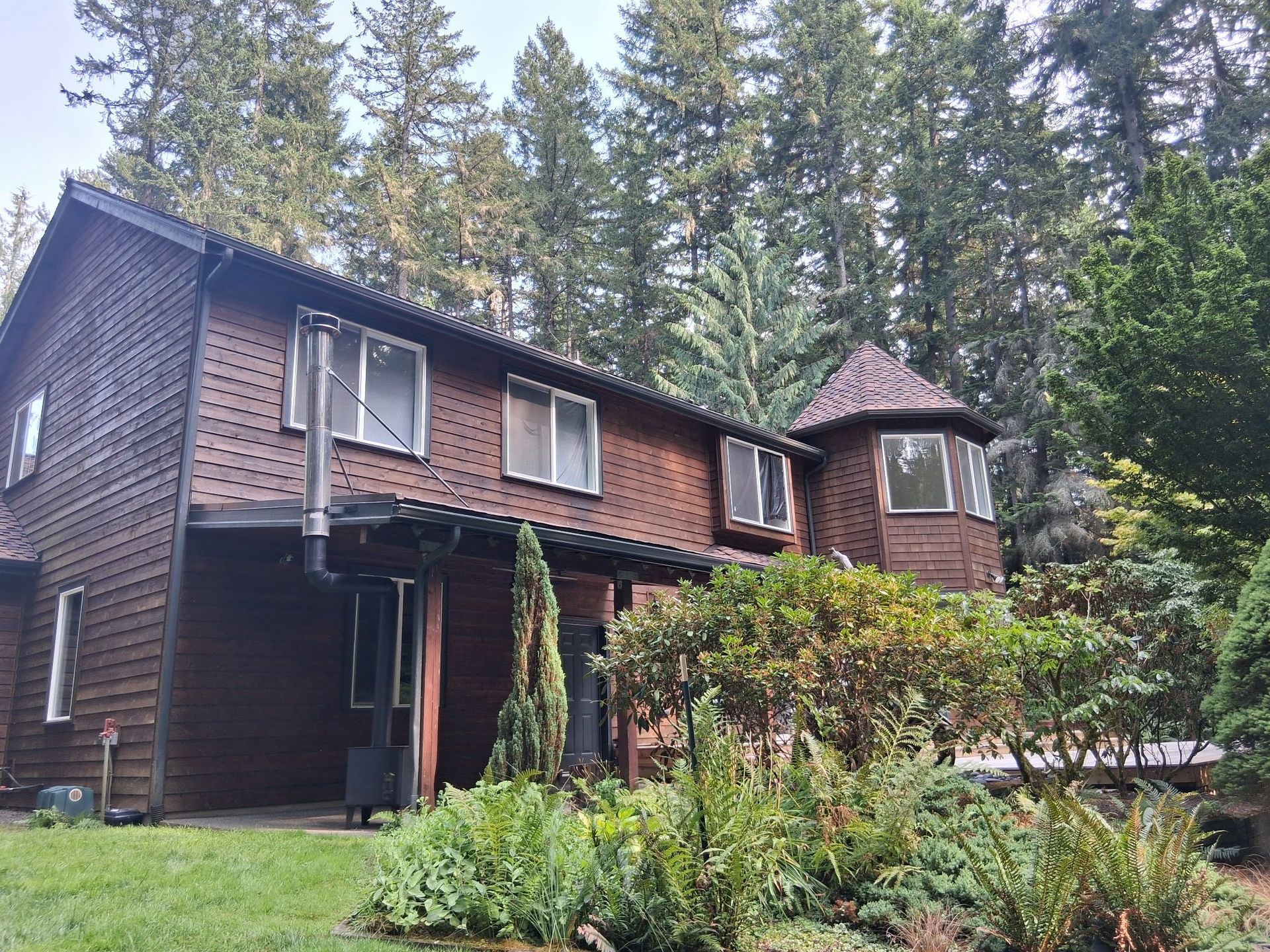 Brown wooden house with turret, surrounded by trees and greenery.