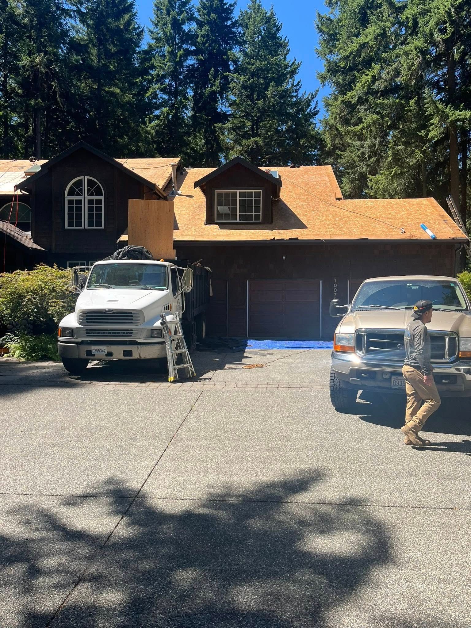 House with a partially replaced roof; construction vehicles and workers on the driveway.
