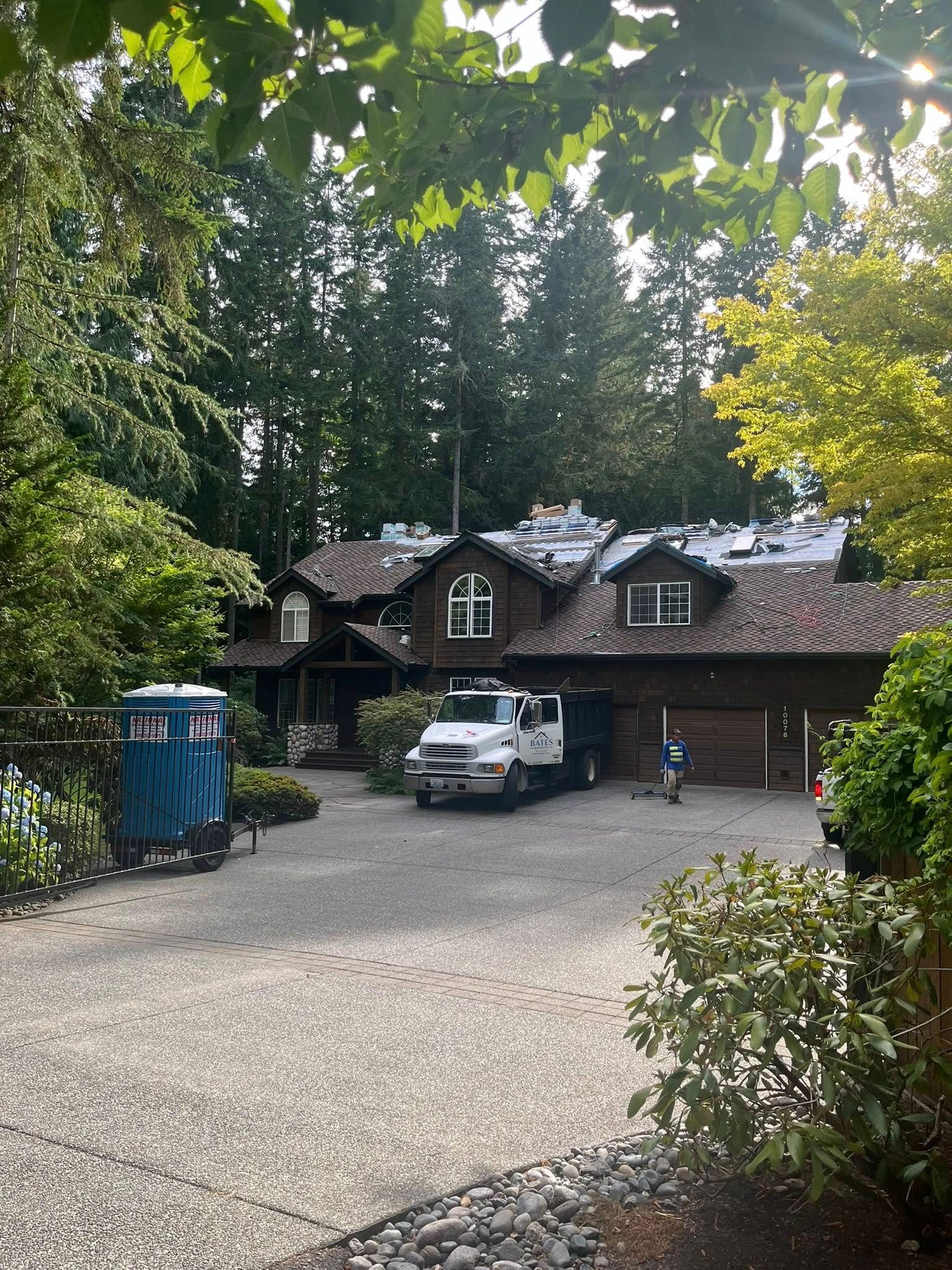 A house with roof work being done, truck parked in front, surrounded by trees.