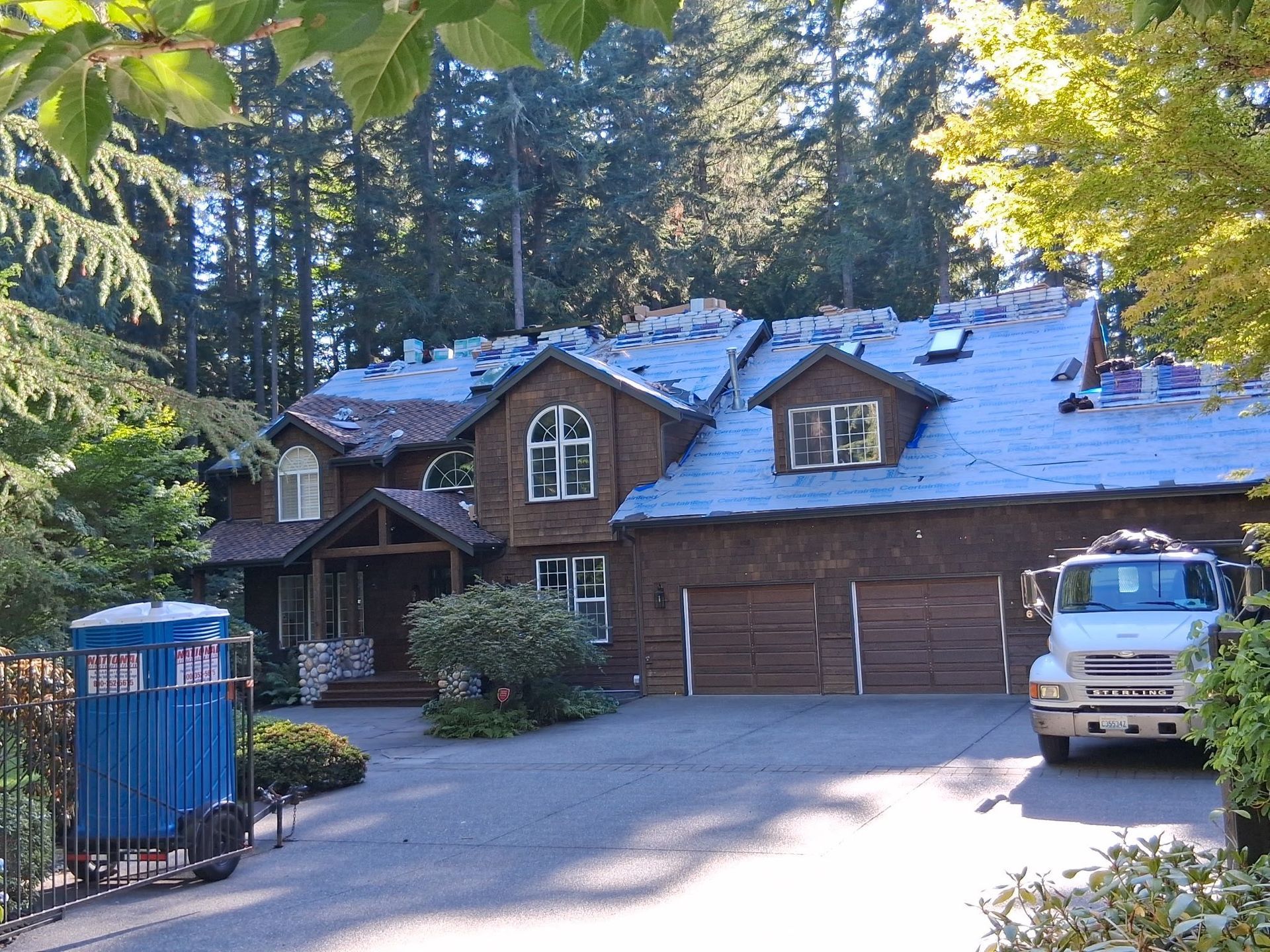 House with roof partially replaced, porta-potty in driveway, truck parked near garage doors.