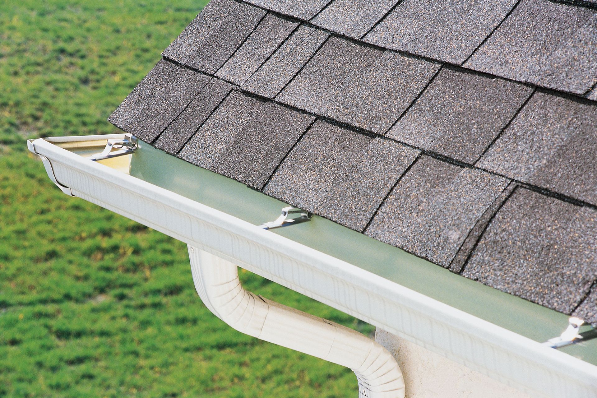 Roof with gray shingles and white gutters. Green grass in the background.