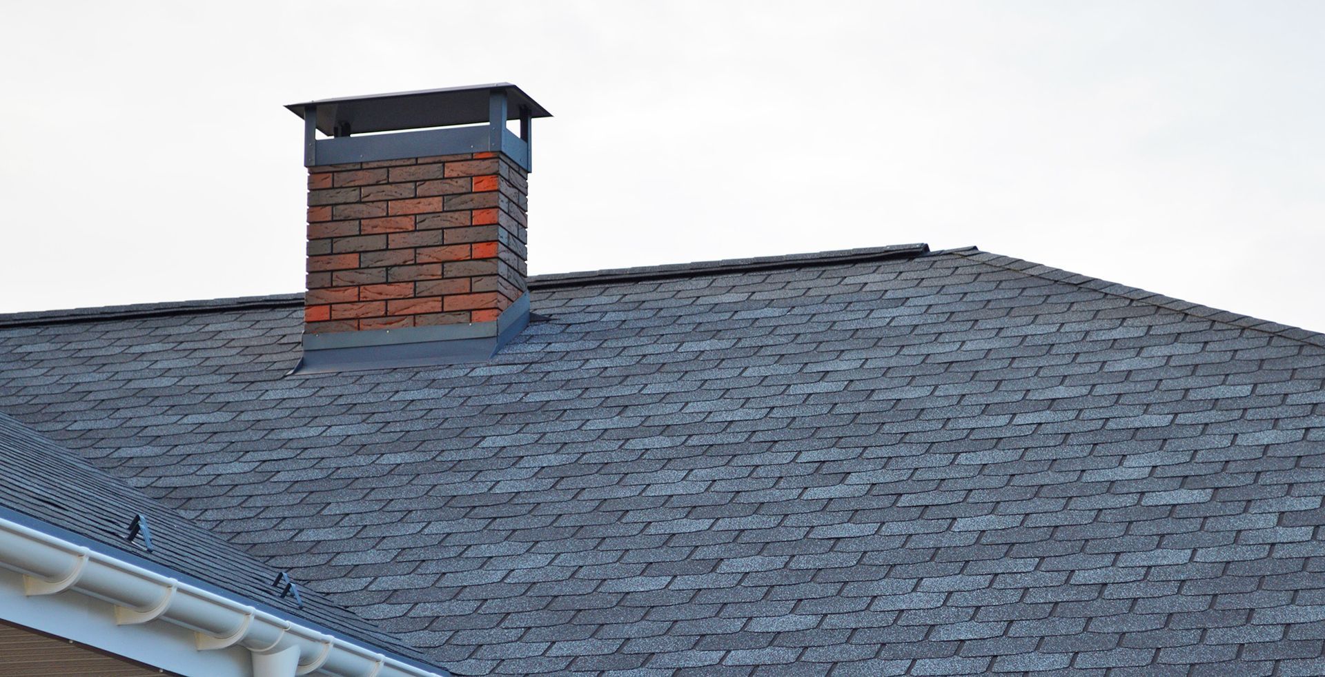 Brick chimney on a gray asphalt shingle roof. White gutters are visible on the lower left.