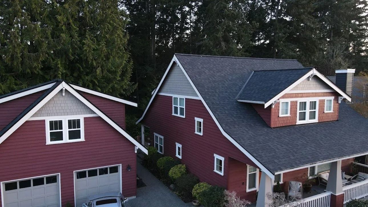 Red-sided house and garage with white trim; gray roof; green trees in the background.
