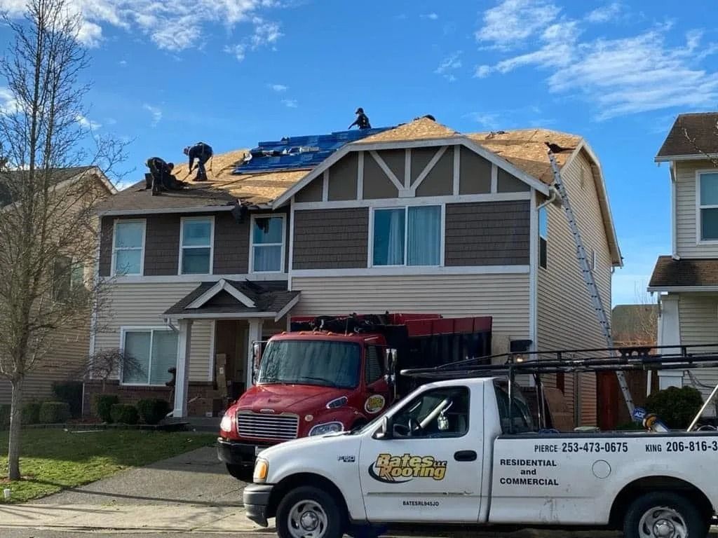 House under roof repair with workers, red truck, white truck parked in front.