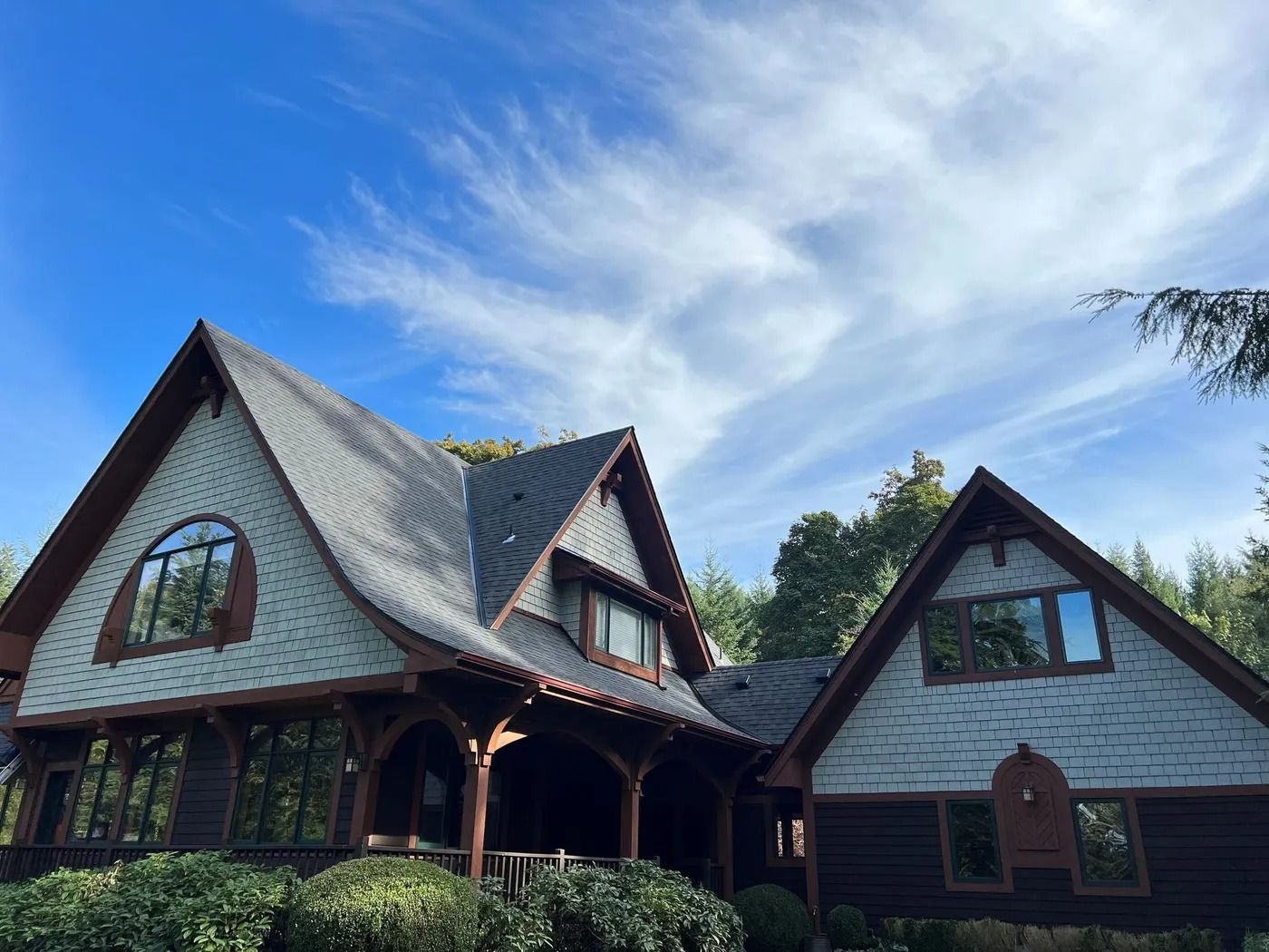 Two-story house with dark brown trim, grey roof, and a blue sky with clouds in the background.