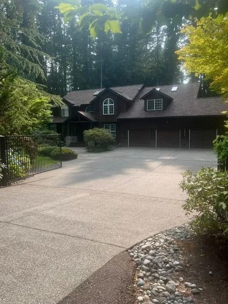 House with a dark roof and three-car garage, long driveway, and surrounding trees.