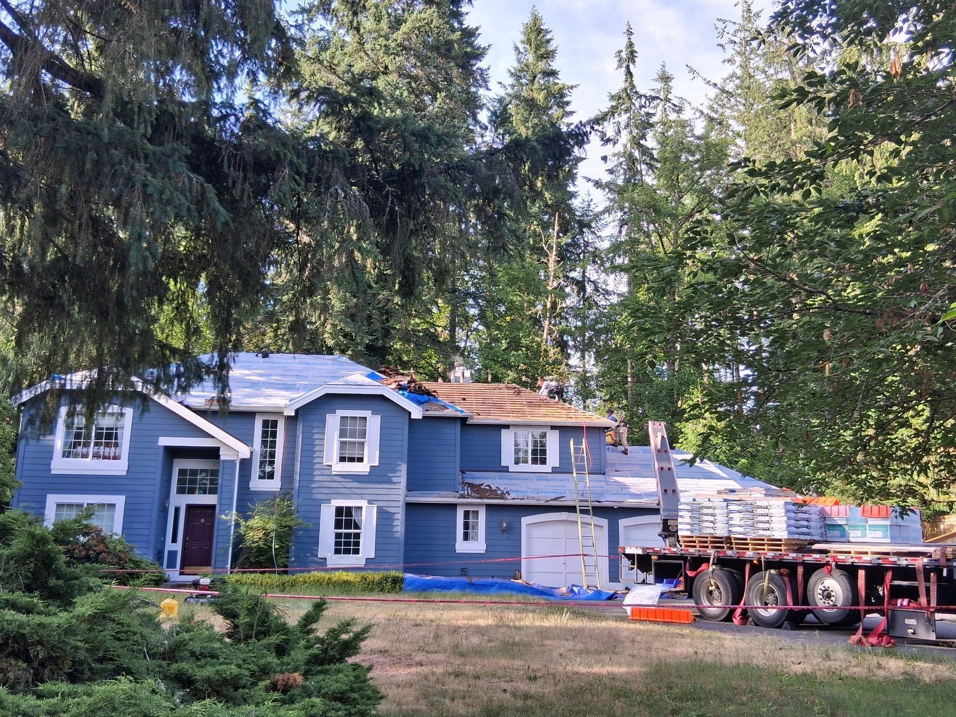 Blue house with partially removed roof, construction materials, and truck; trees in the background.
