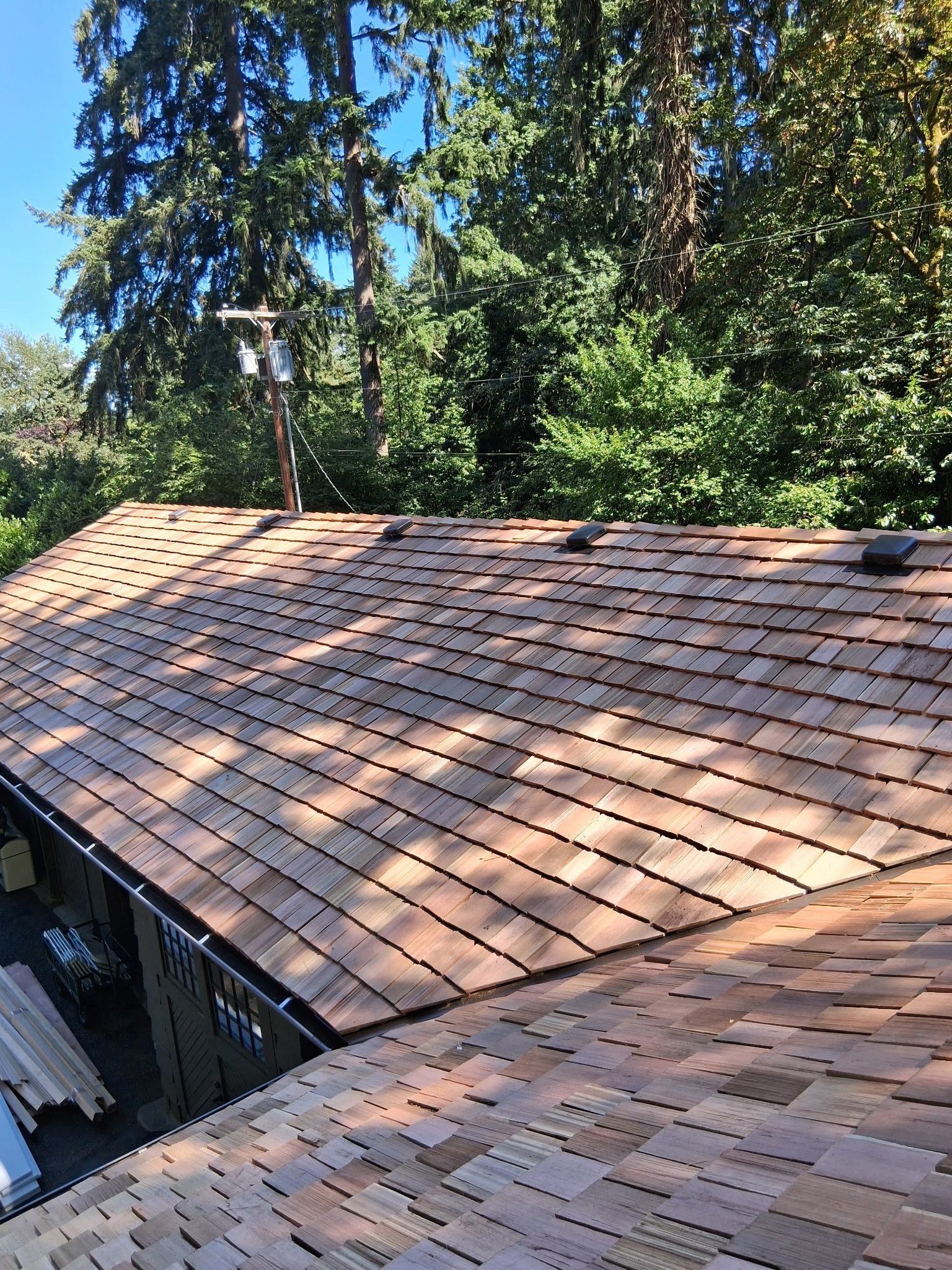 Cedar shake roof with trees in background on a sunny day.