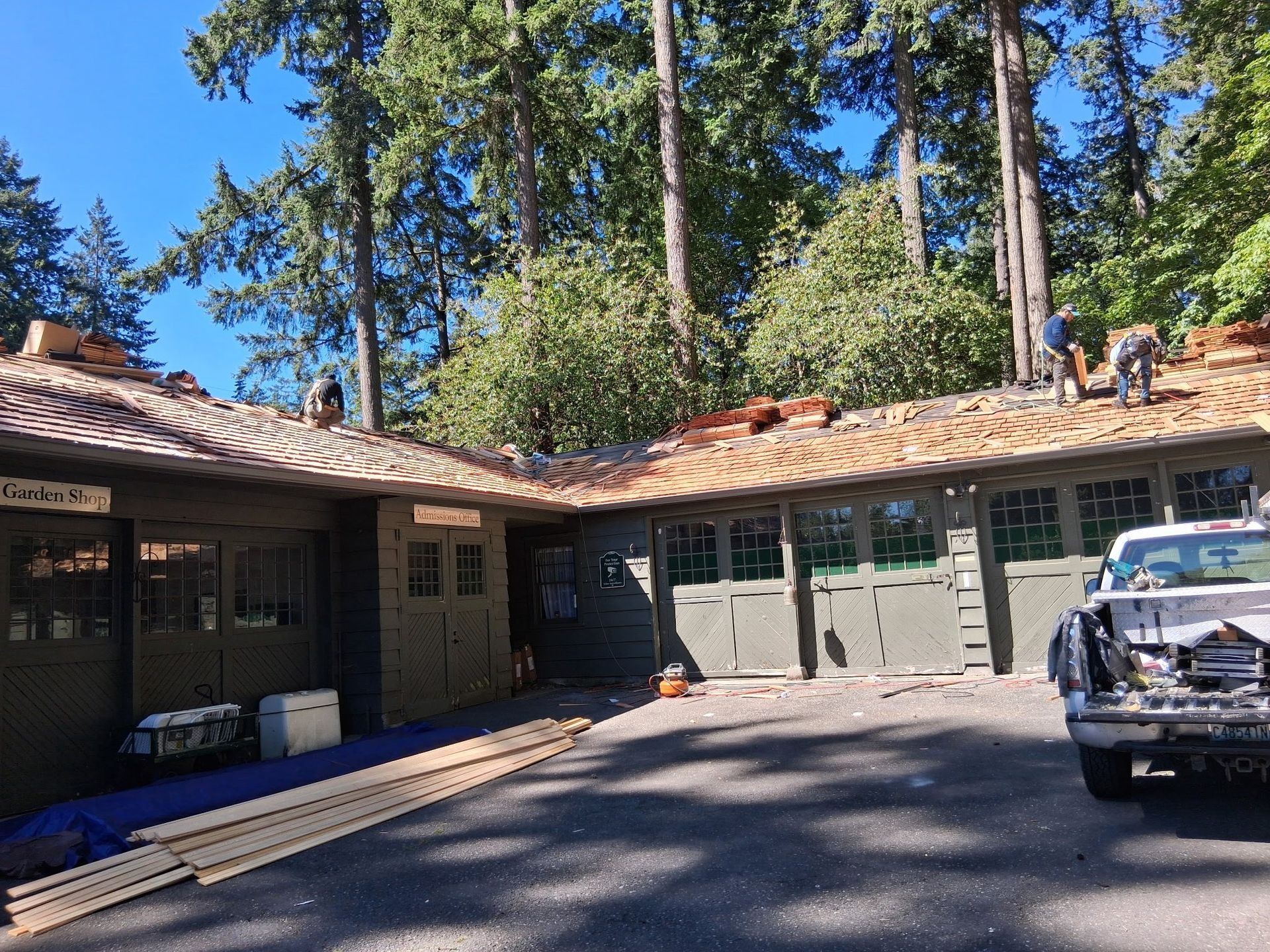 Workers replacing roof tiles on a building with green siding, under a clear blue sky.