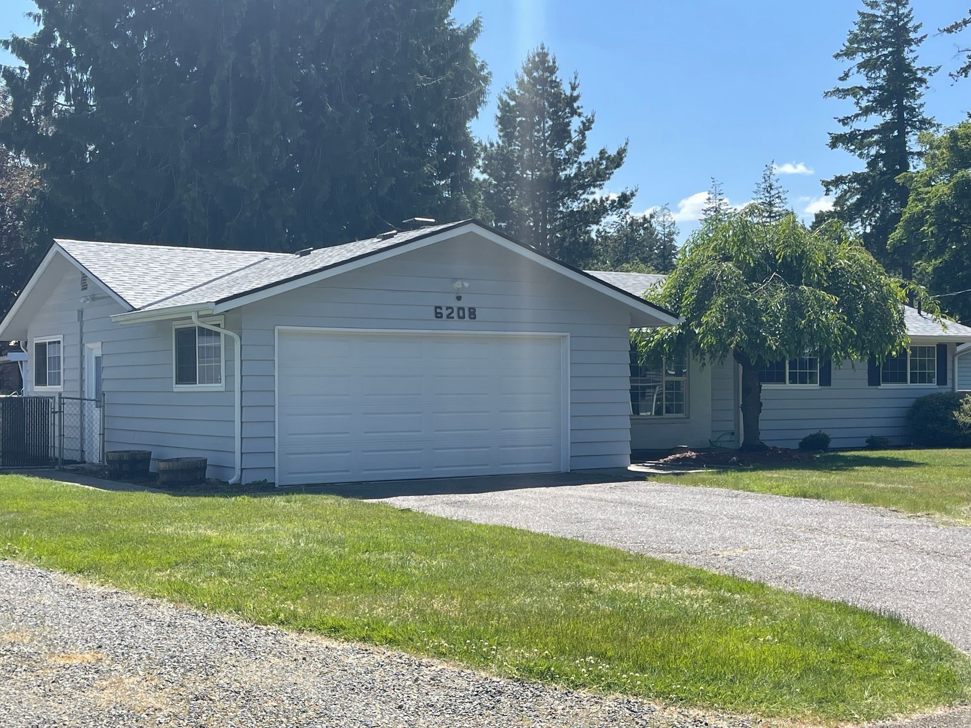 Light blue house with attached garage and driveway on a sunny day. Green grass and trees are in the yard.