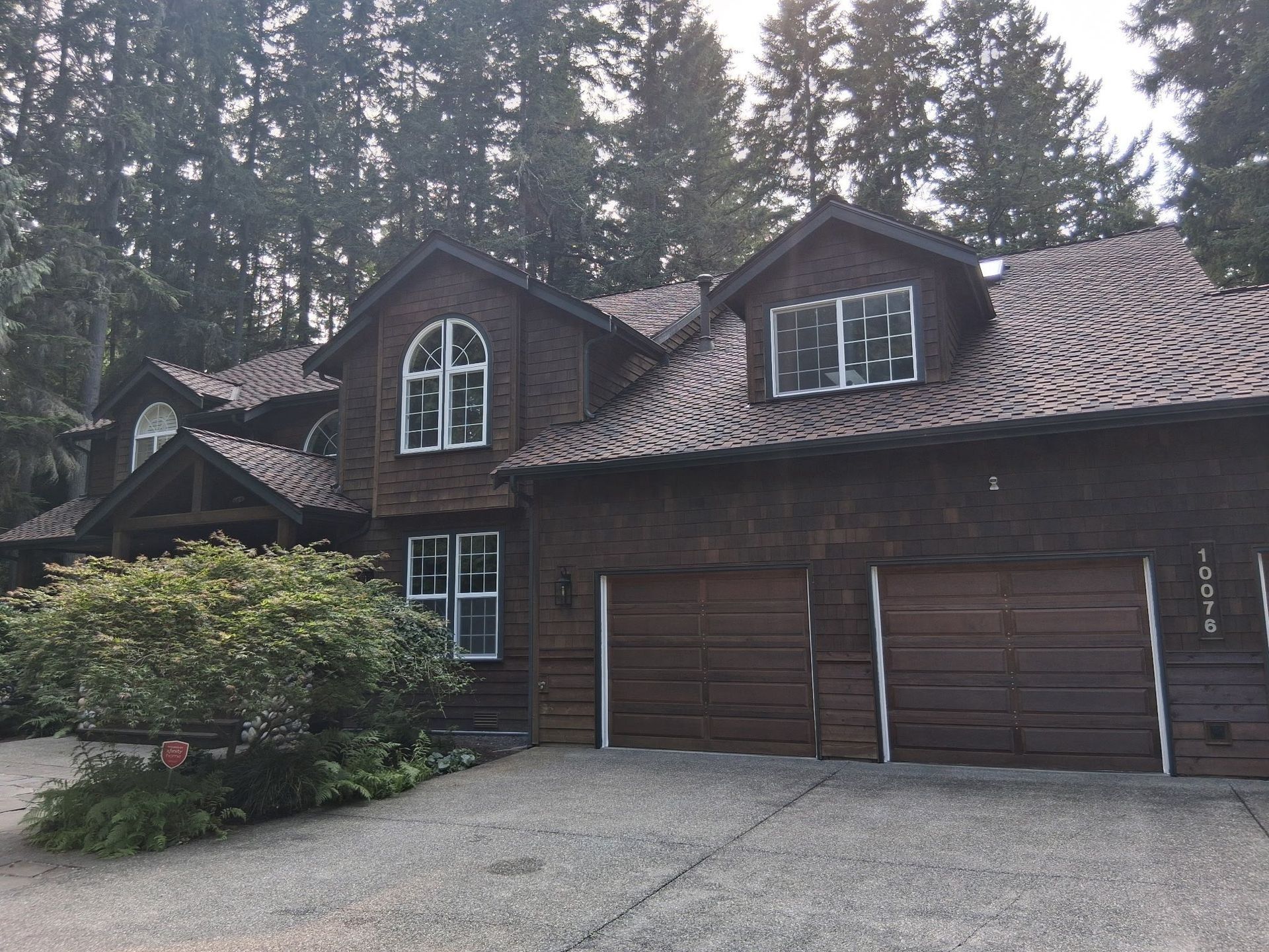 Brown two-story house with a tile roof, two-car garage, and surrounding trees.