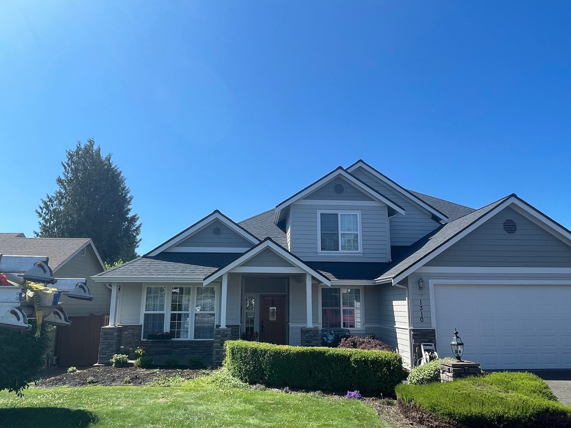 Two-story suburban house with gray siding, blue roof, manicured lawn, and clear blue sky.