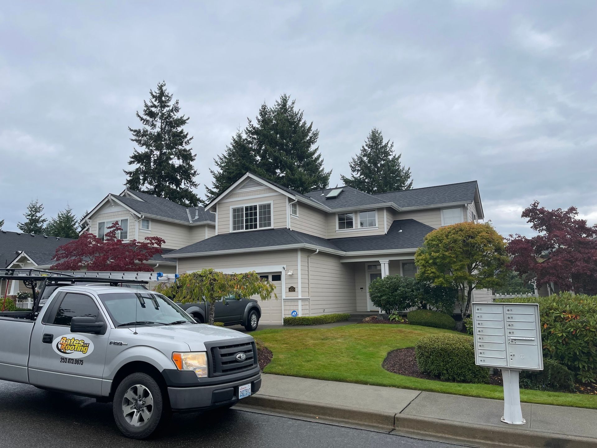 Gray Ford truck parked in front of a light-colored house with a dark roof on an overcast day.