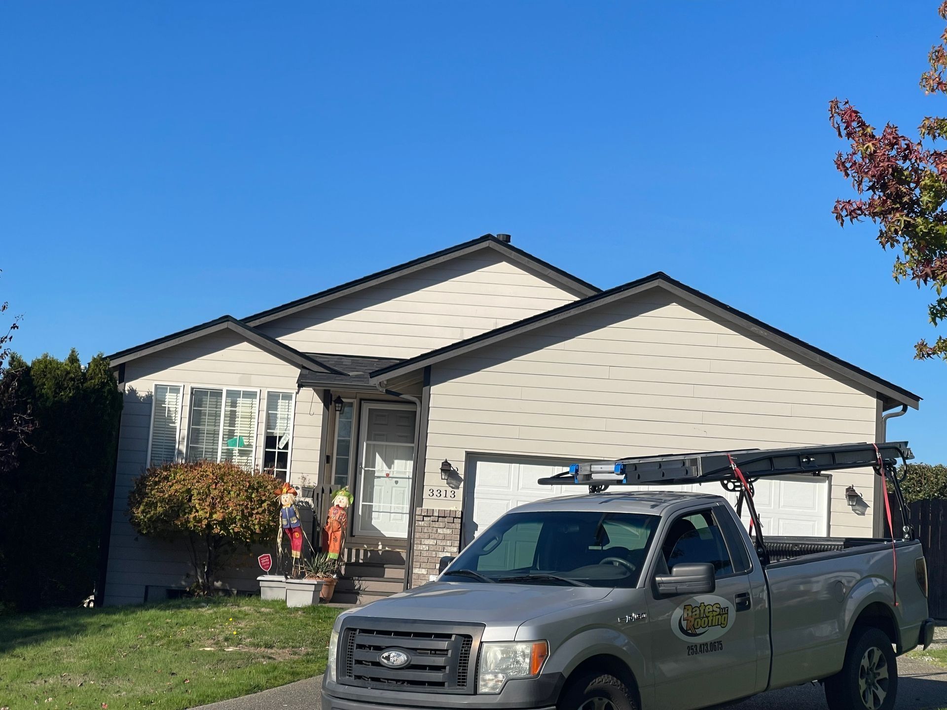 Gray pickup truck parked in front of a house with beige siding and a dark roof under a blue sky.