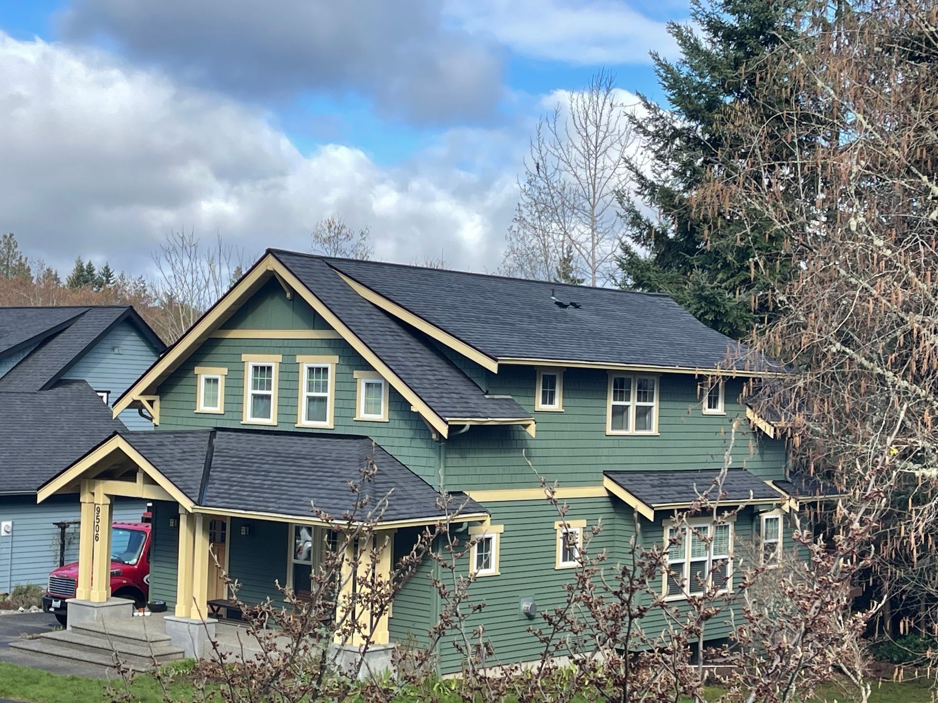 Green house with dark roof and cream trim under a partly cloudy sky.