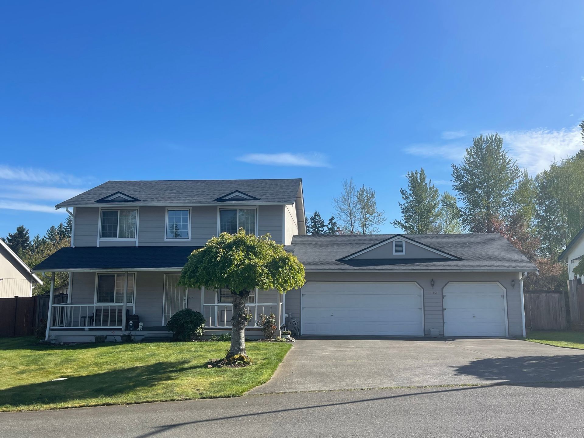 Two-story gray house with a three-car garage, green lawn, and blue sky.