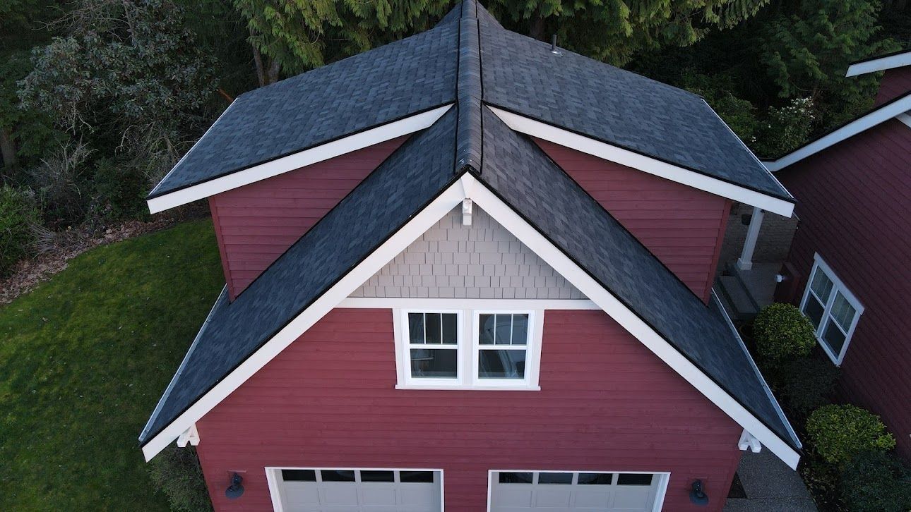 Red house with dark roof and white trim. Two garage doors below two windows.