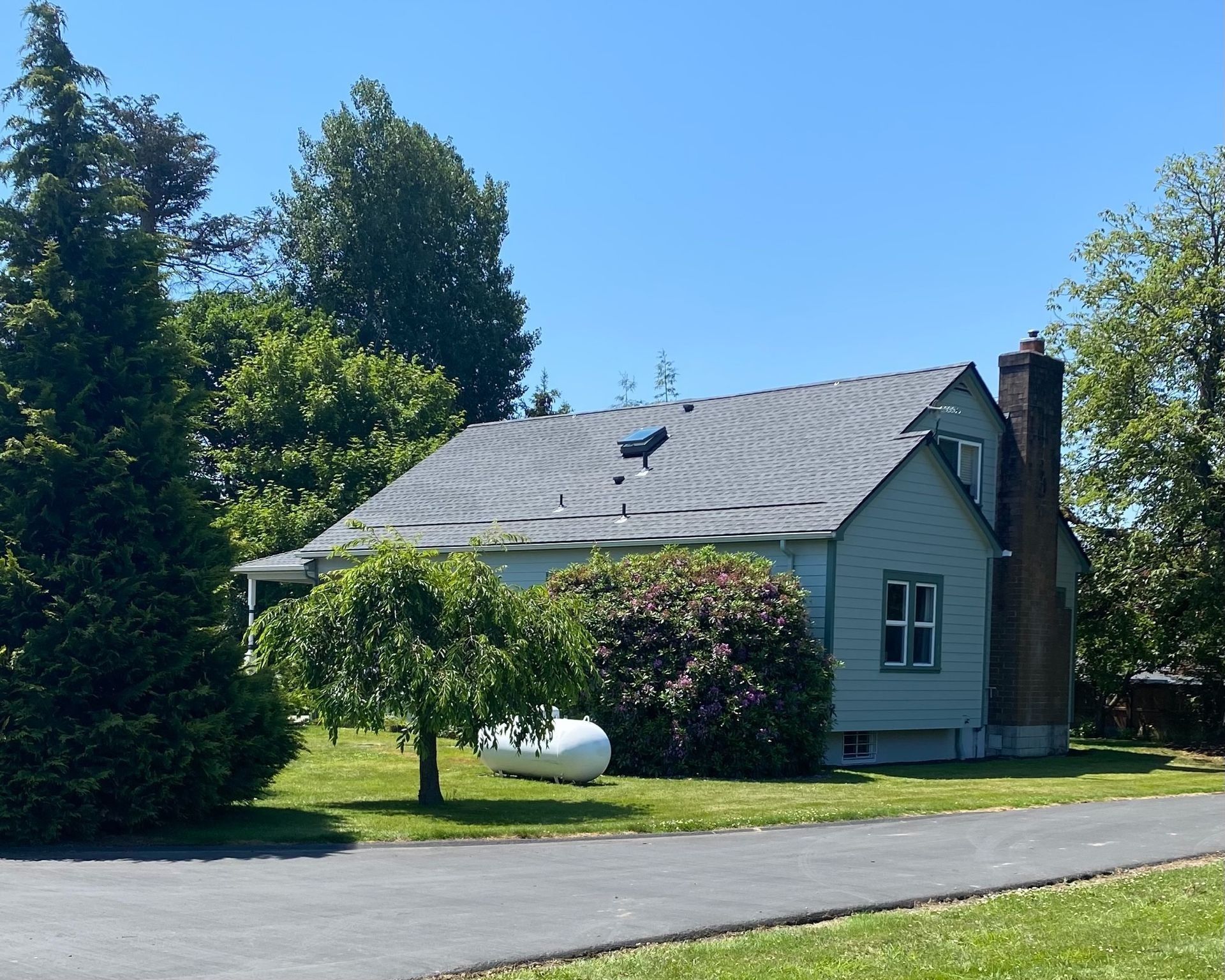 A light blue house with a gray roof and a brick chimney sits on a grassy lot.
