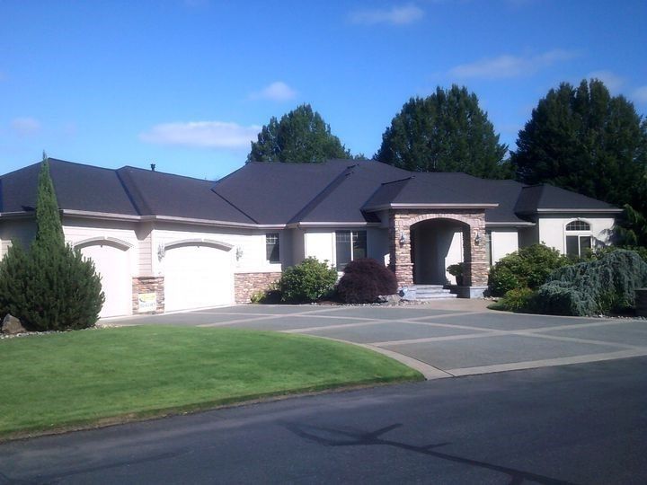Beige and brick home with black roof, two-car garage, and arched entrance on a sunny day.