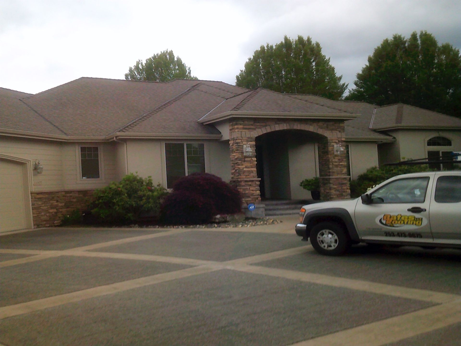 Tan house with stone accents, arched entryway, and a silver pickup truck parked out front.