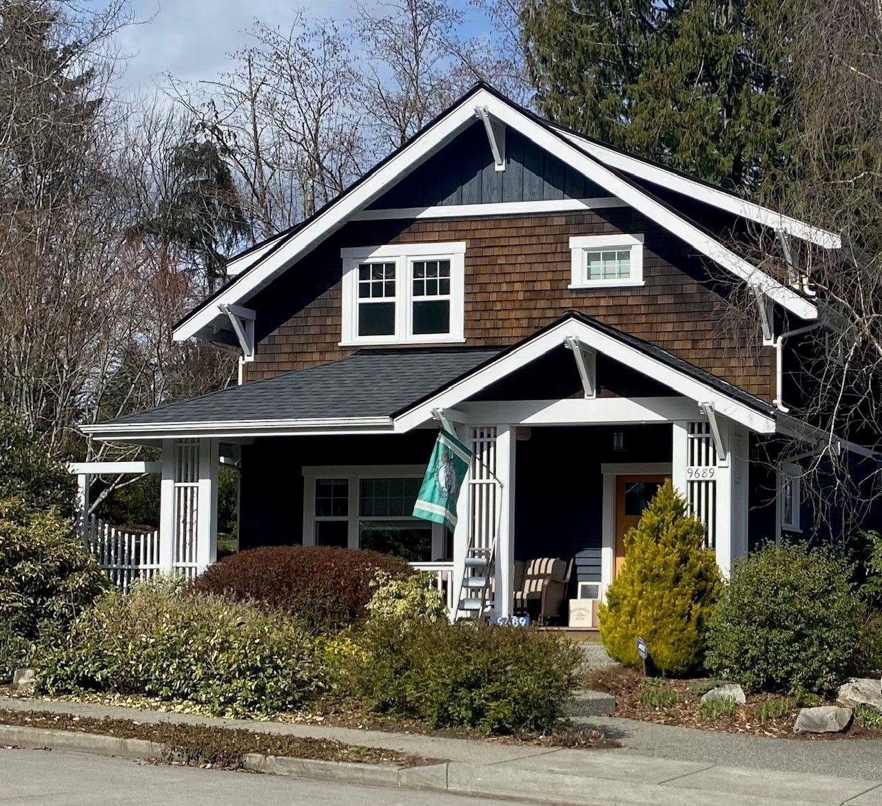 Cottage-style home with dark brown siding, white trim, and a small front porch. Bushes and trees in front.