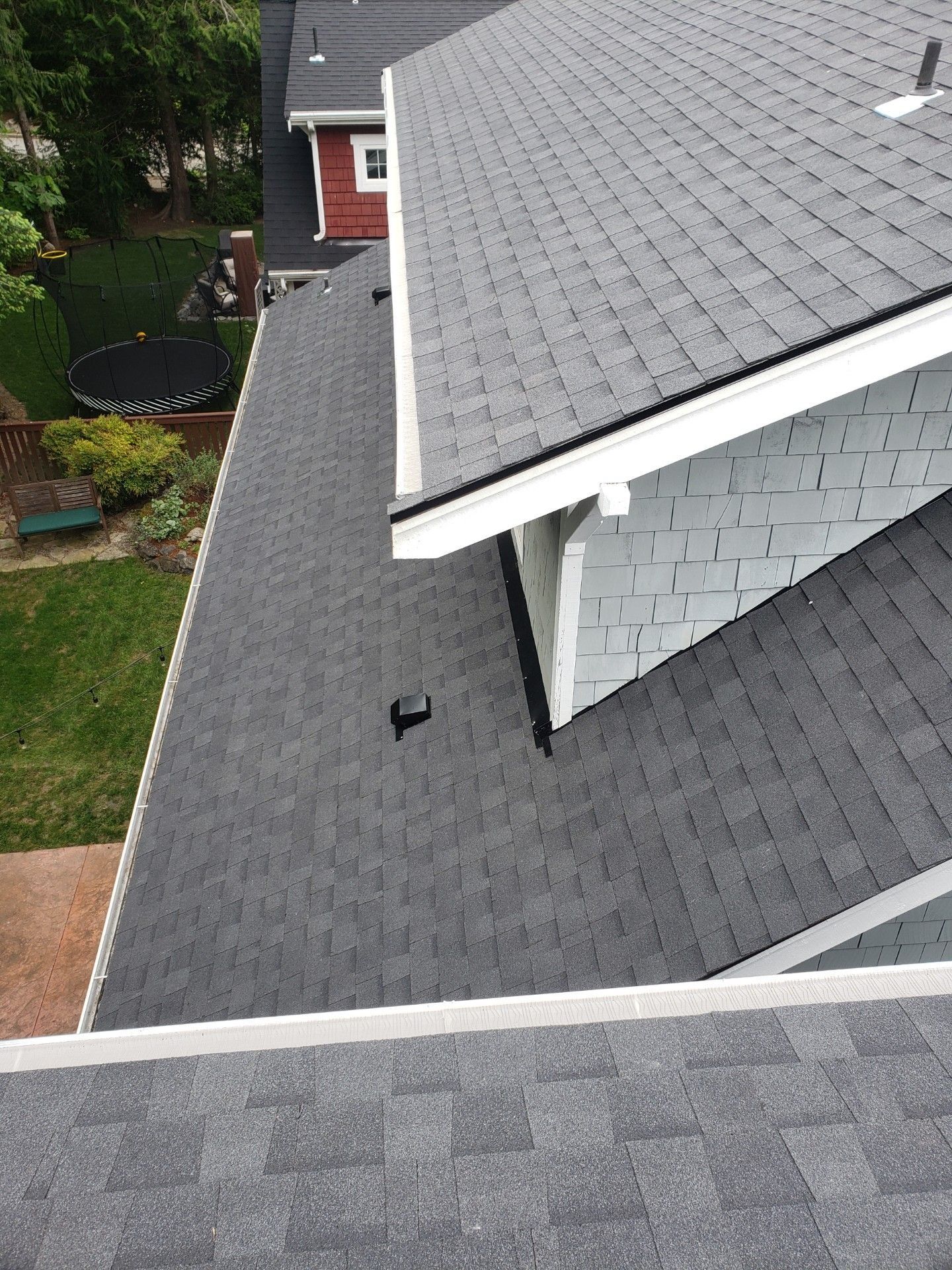 Newly shingled gray asphalt roof on a house, viewed from above, with a white trim.