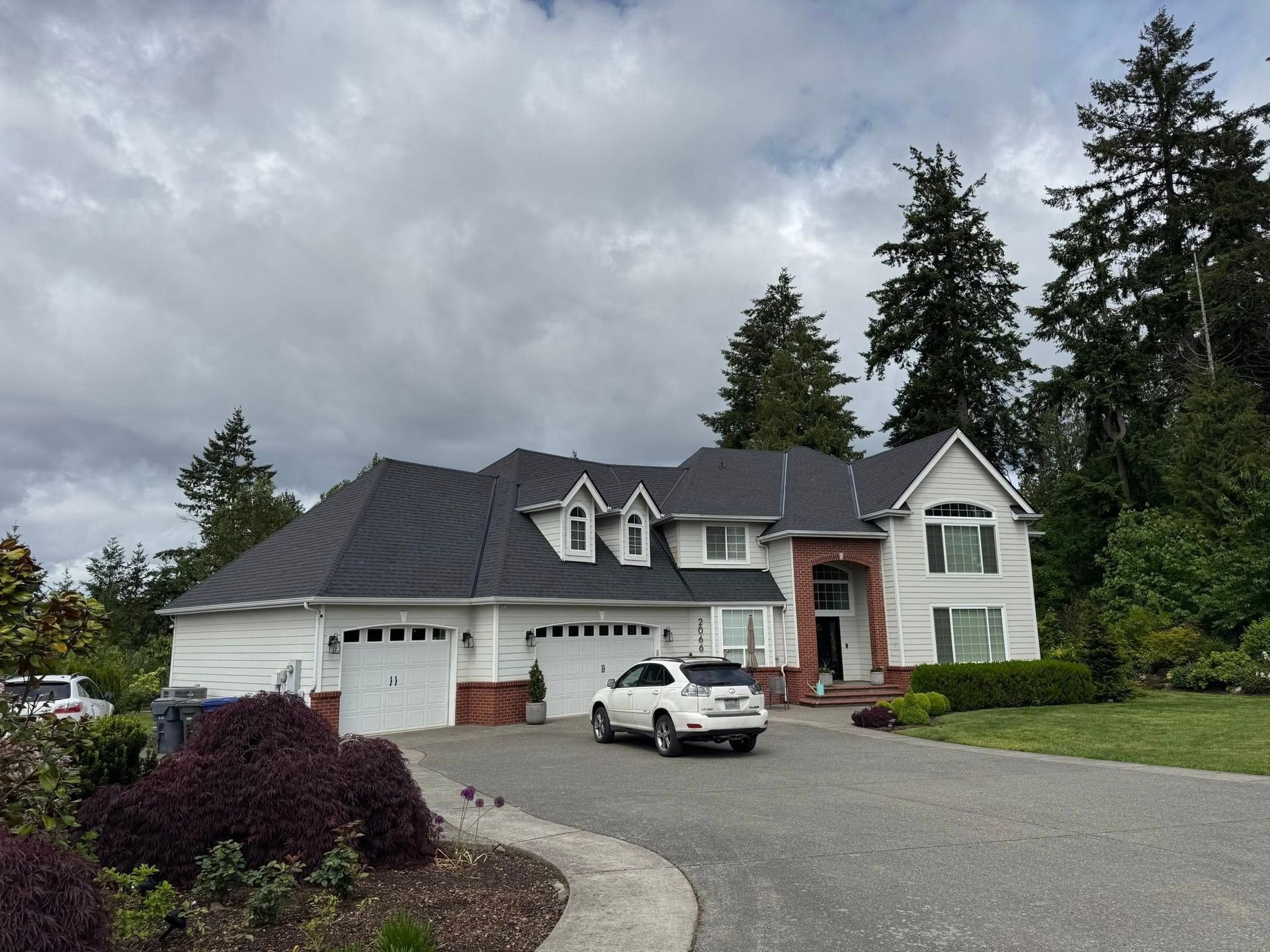 White house with black roof, three-car garage, and a car in the driveway on a cloudy day.
