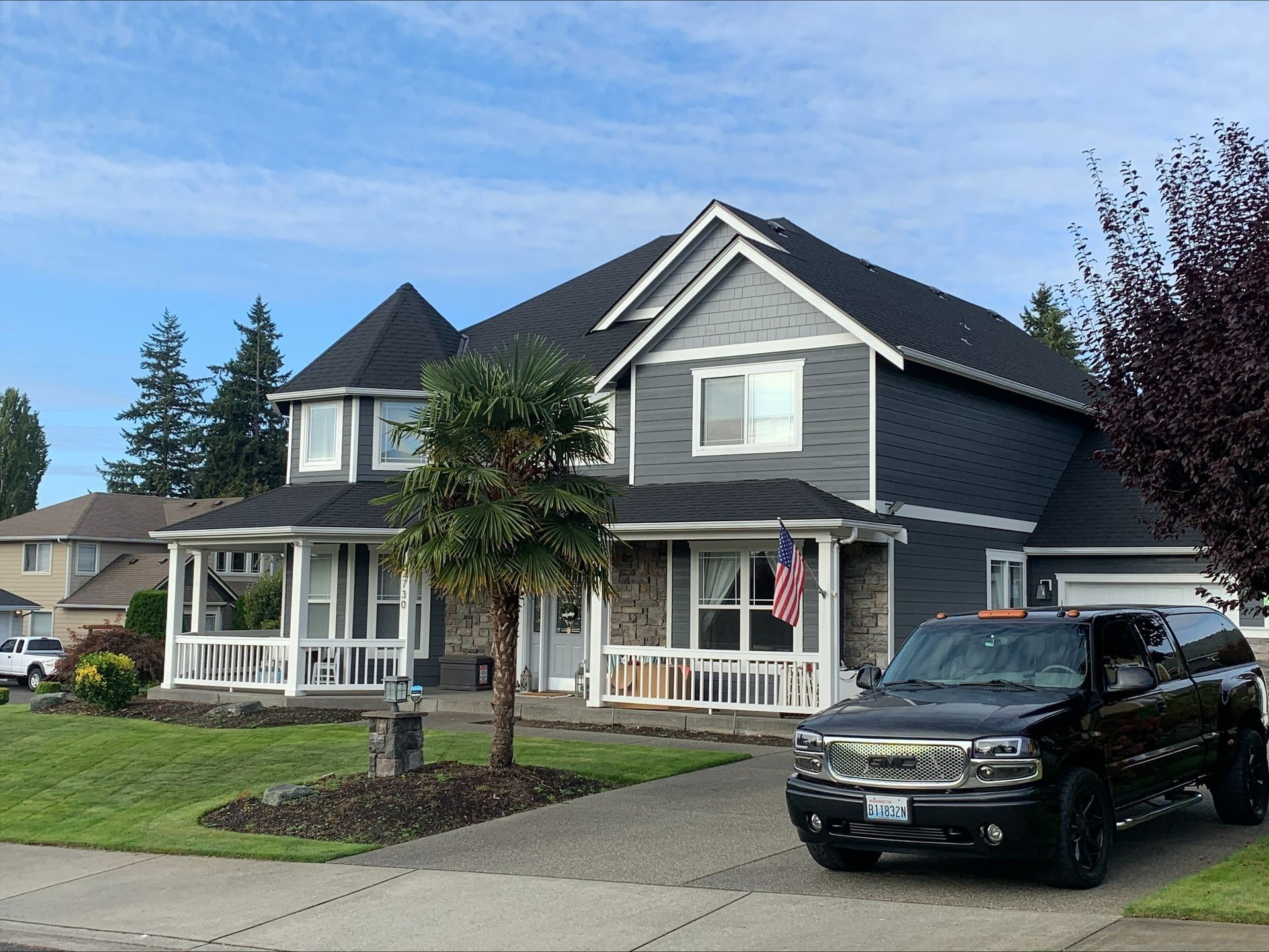 Two-story house with gray siding, a black SUV parked in the driveway, and a small American flag hanging from the porch.
