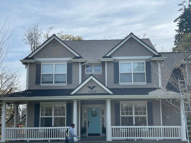 Two-story house with light brown siding, black shutters, and a blue front door.