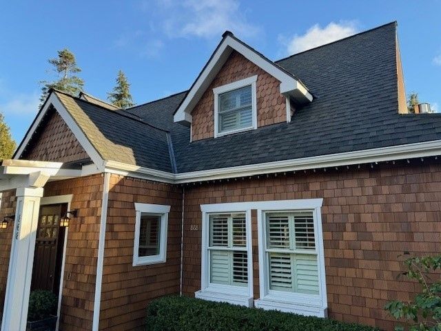 Brown house with dark roof and white trim under a blue sky.