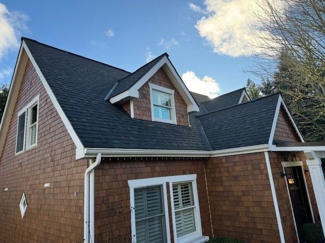 Brown house with dark roof and white trim under a partly cloudy blue sky.