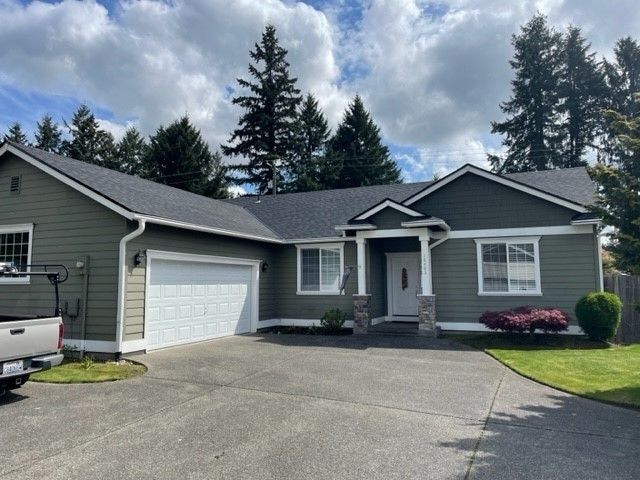 Green house with white garage door and concrete driveway.