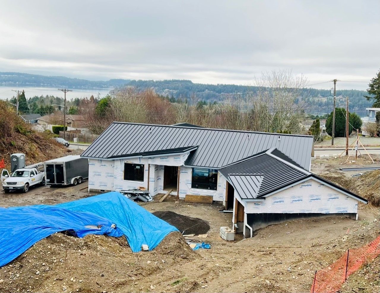 House under construction with metal roof, tarp, and view of water and hills.