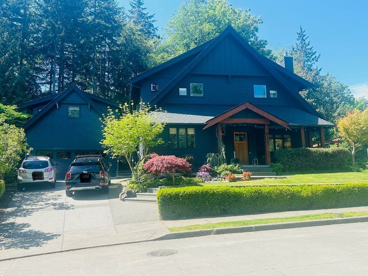 Dark blue house with attached garage, cars in the driveway, and green lawn with trimmed bushes.