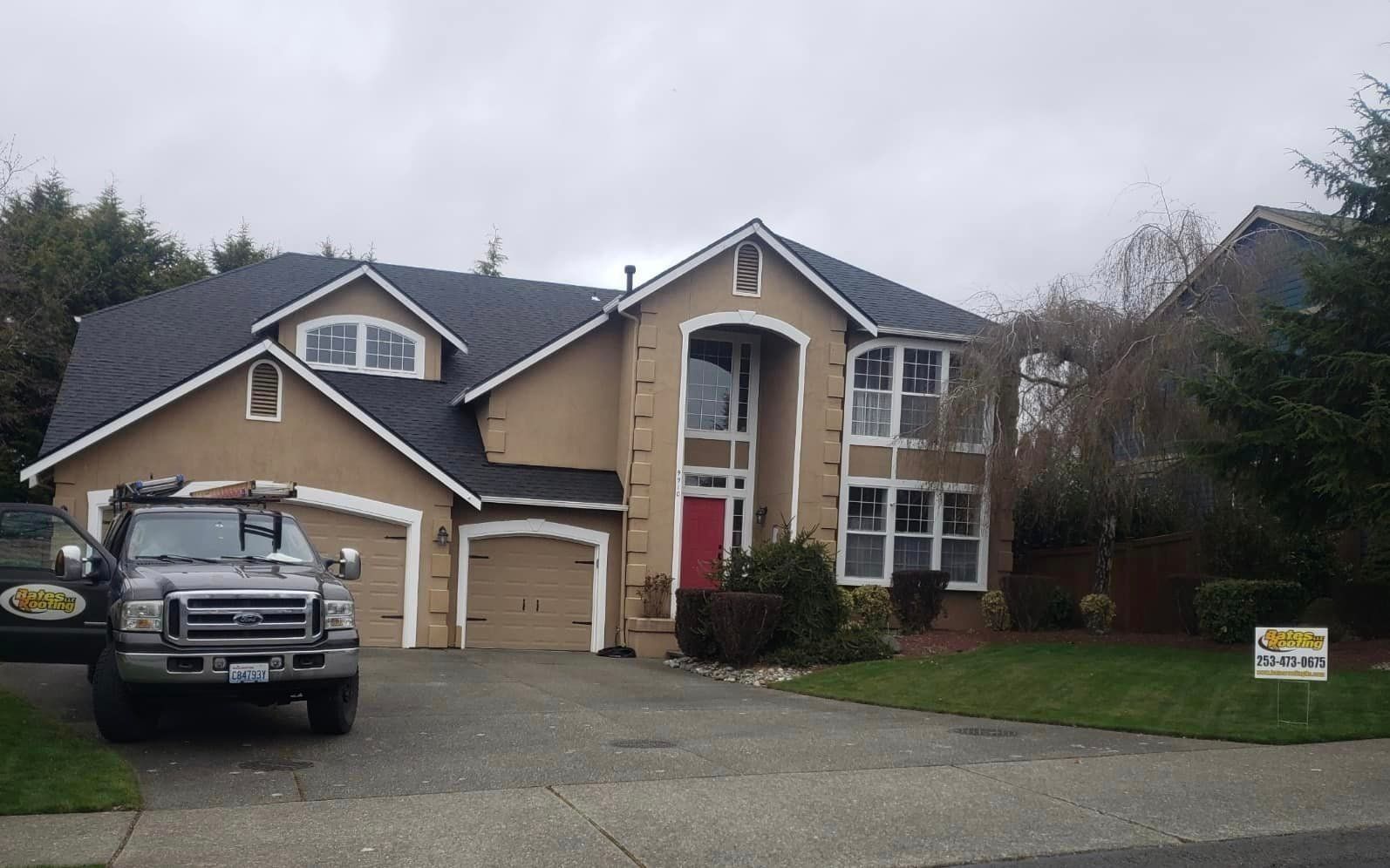 Tan two-story house with black roof, red front door, and a pickup truck parked in front.