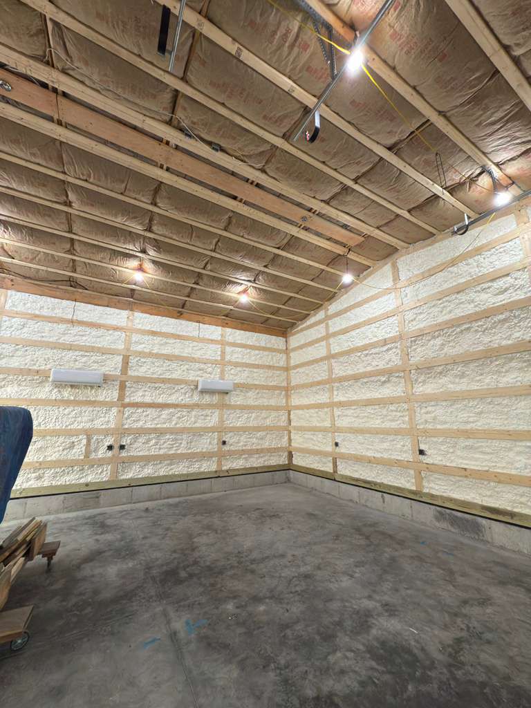 Interior of a building with exposed wooden beams and spray foam insulation, concrete floor, and air conditioning units.