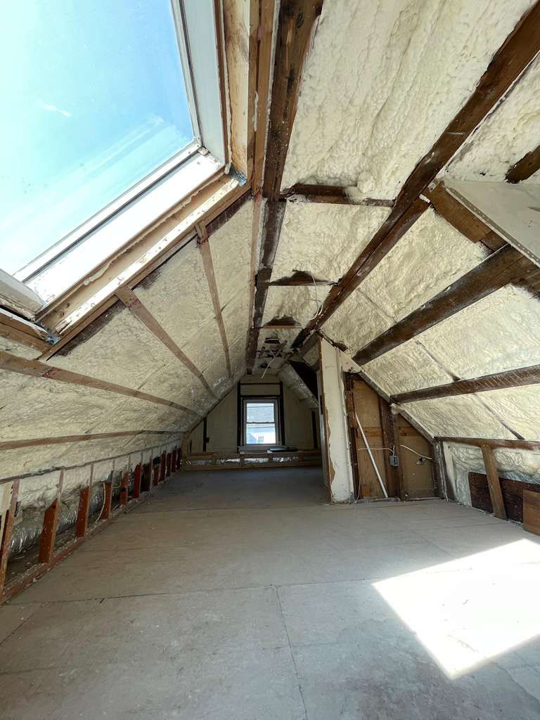 Attic interior with exposed beams, spray foam insulation, and a skylight.