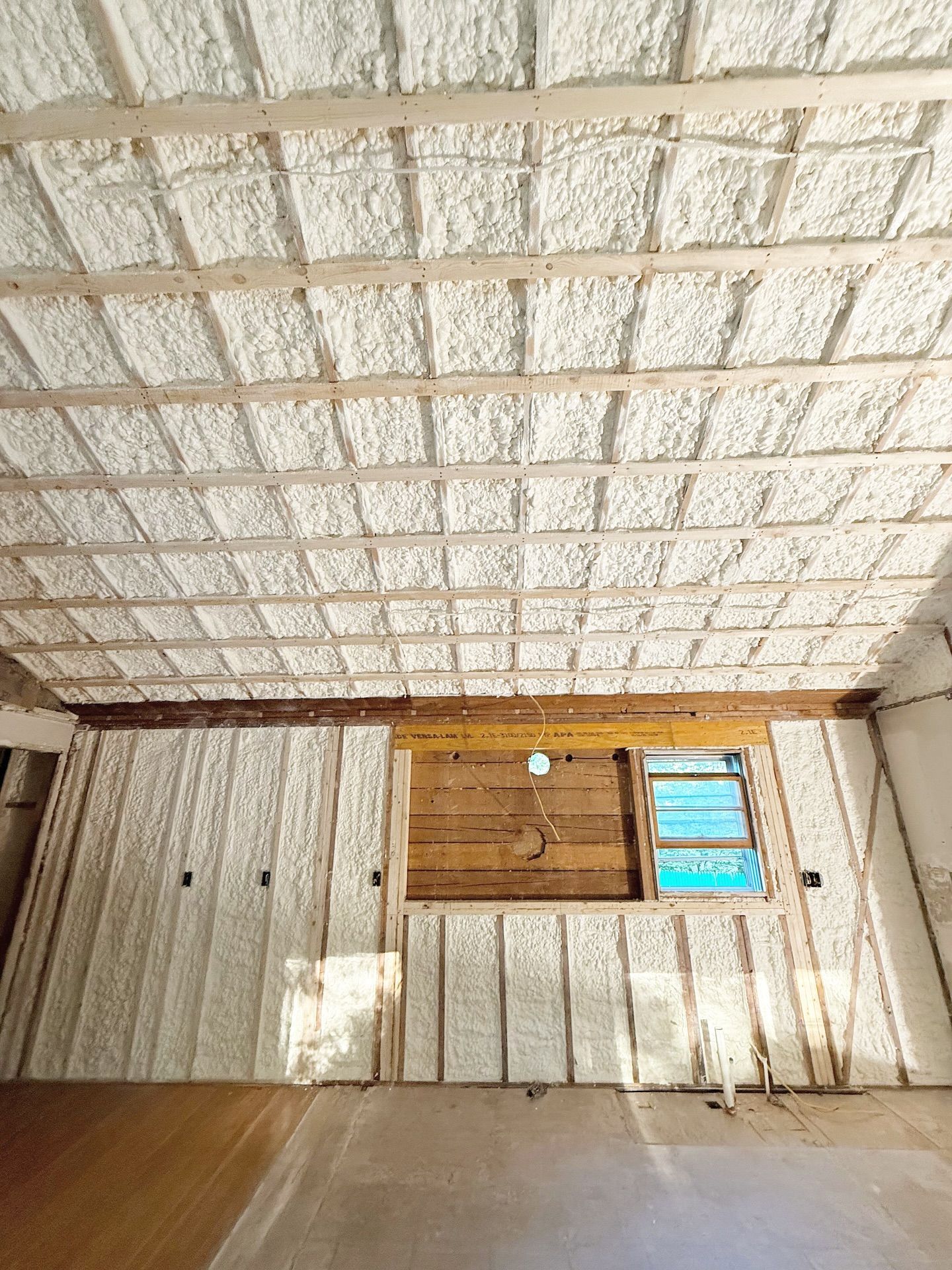 Interior of a room with spray foam insulation on the ceiling and walls, wood framing visible.