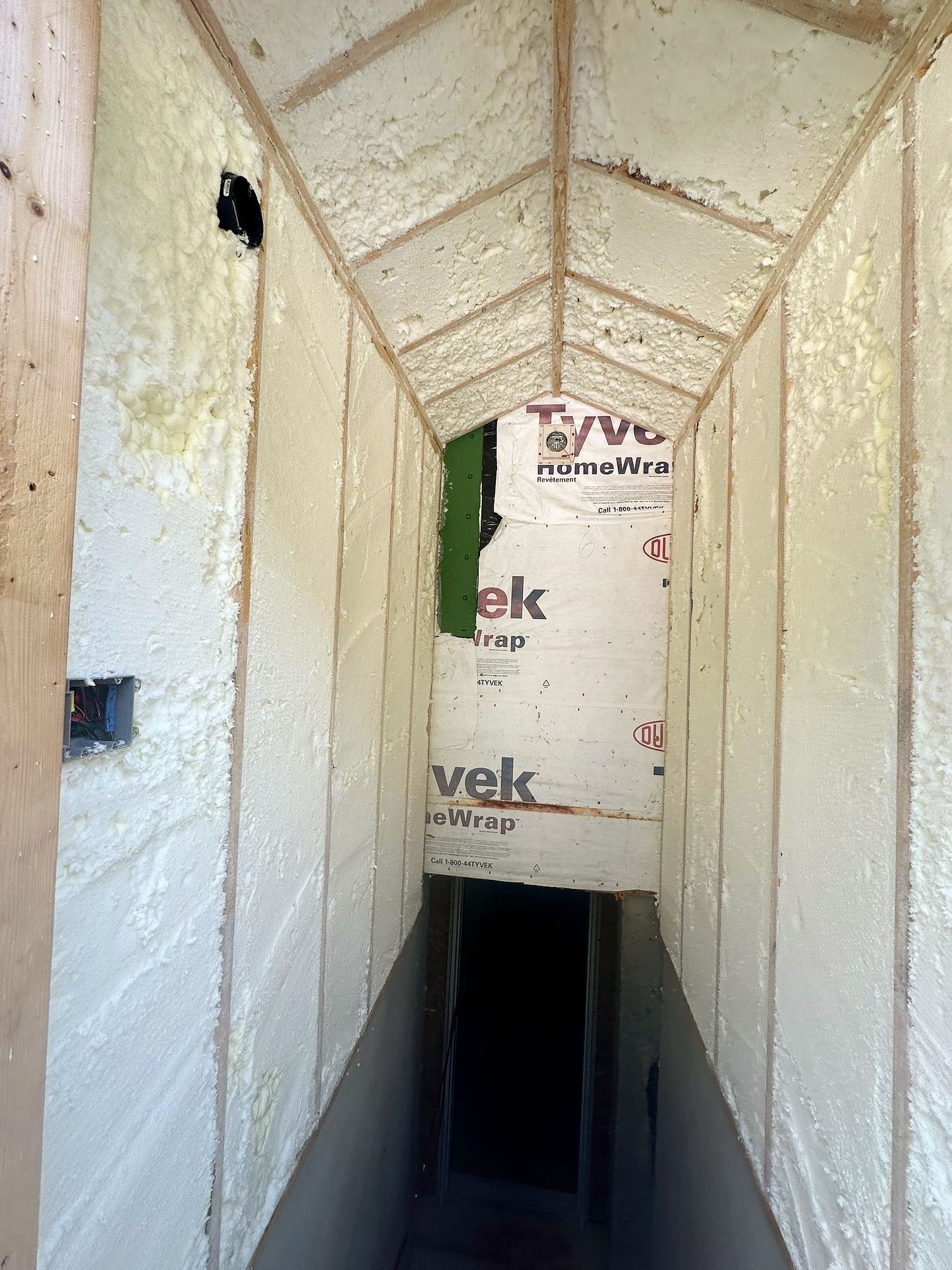 Tunnel-like entry with white foam insulation on walls and ceiling; dark opening at the end.