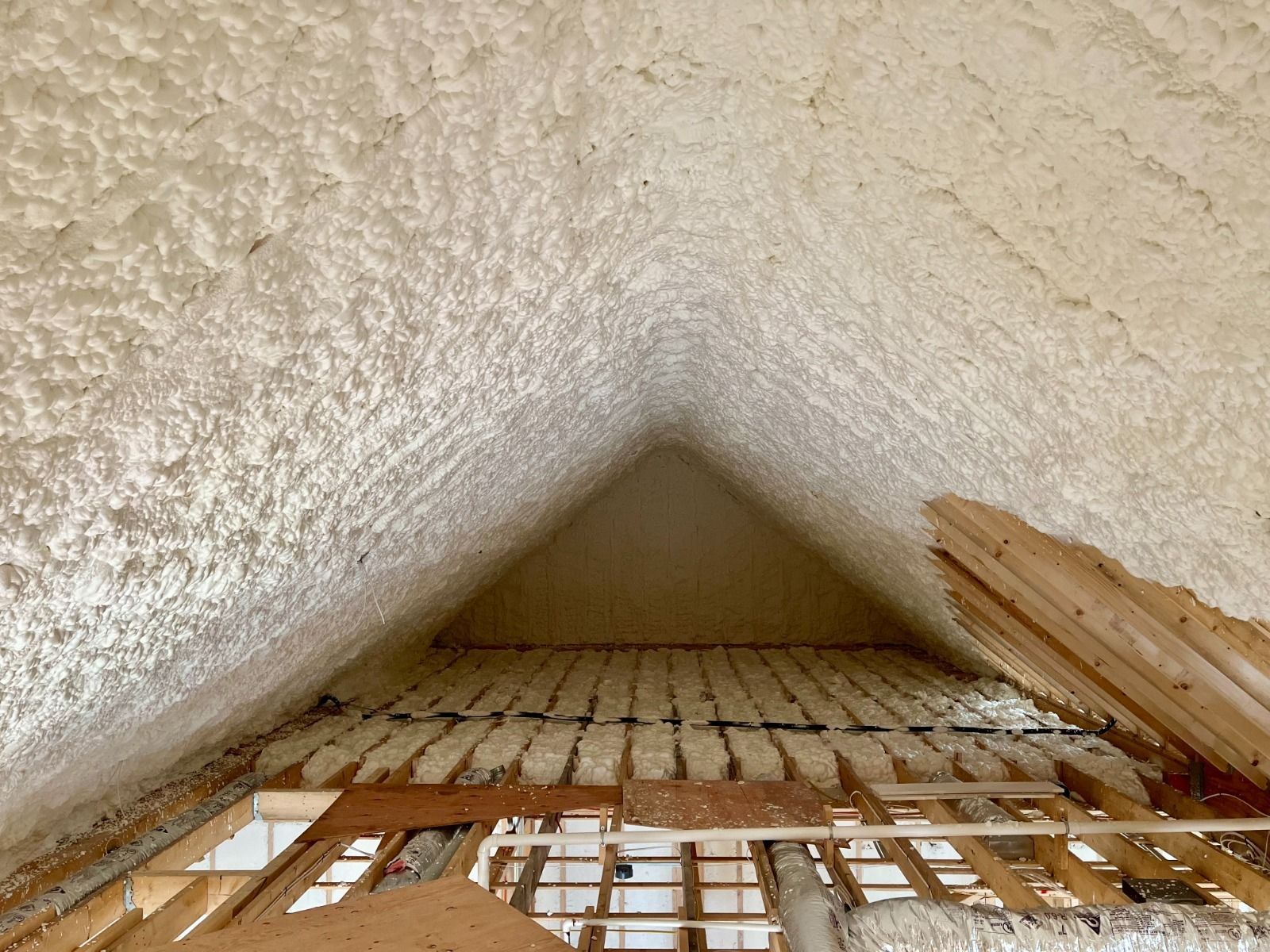 Spray foam insulation covering an attic's roof and rafters, appearing white/tan against exposed wood framing.